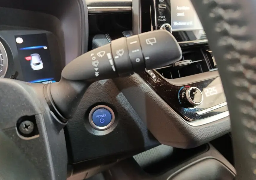 Détail intérieur du tableau de bord de la Toyota Corolla Hybride 122h 2020 avec bouton démarrage bleu et commandes de climatisation.