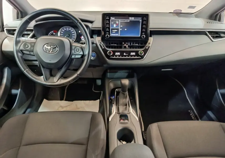 Vue intérieure avant de la Toyota Corolla Hybride 122h, tableau de bord avec écran tactile et volant multifonctions cuir noir.