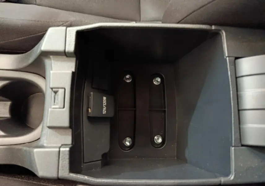 Vue plongeante sur le rangement central noir de la Toyota Corolla Hybride 122h Active, avec prise 12V visible.