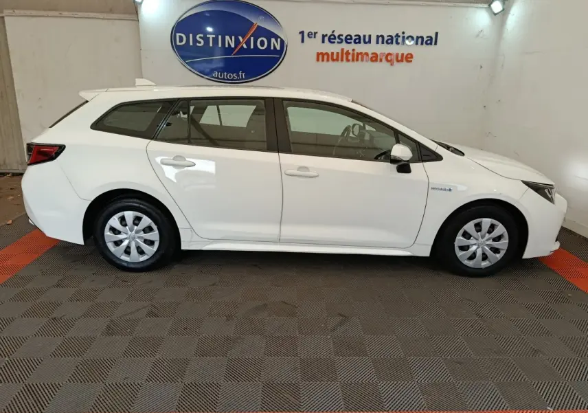 Vue latérale droite d'une Toyota Corolla Hybride 122h Active blanche en version break, avec jantes acier et badges hybrides visibles.
