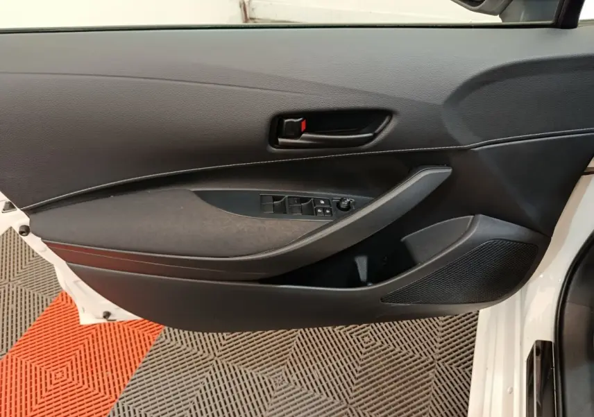 Vue intérieure côté gauche de la porte avant d’une Toyota Corolla Hybride blanche, avec commandes de vitres et poignée noire.