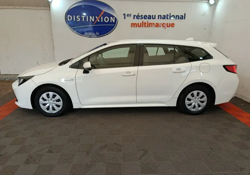 Profil côté gauche d'une Toyota Corolla Hybride 122h Active blanche, break avec jantes acier et rétroviseurs blancs.