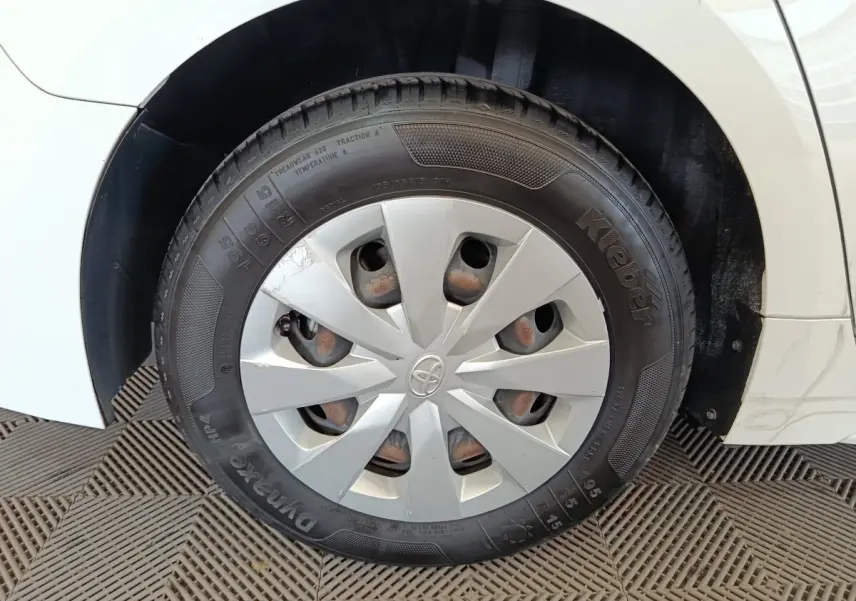 Gros plan sur la roue avant gauche blanche d'une Toyota Corolla Hybride 122h Active, avec enjoliveur argenté et logo Toyota.