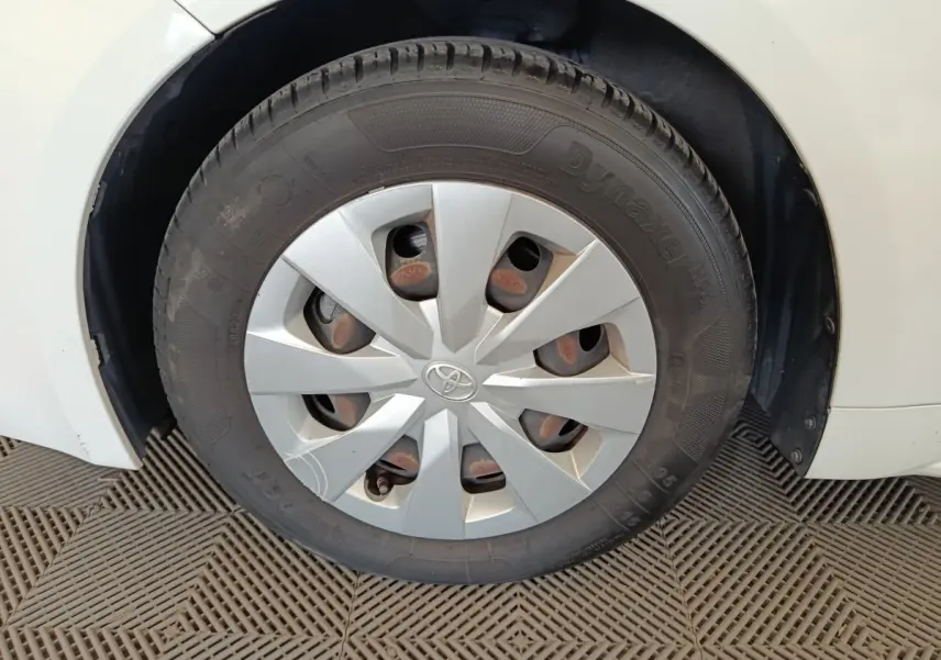 Gros plan sur la roue avant droite d'une Toyota Corolla Hybride blanche, avec enjoliveur gris et logo Toyota central.