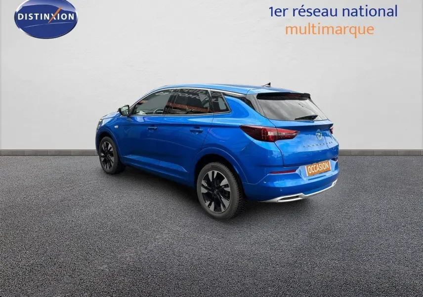 Vue 3/4 arrière droite d'un Opel Grandland bleu Spektrum métal avec jantes noires sur fond neutre.
