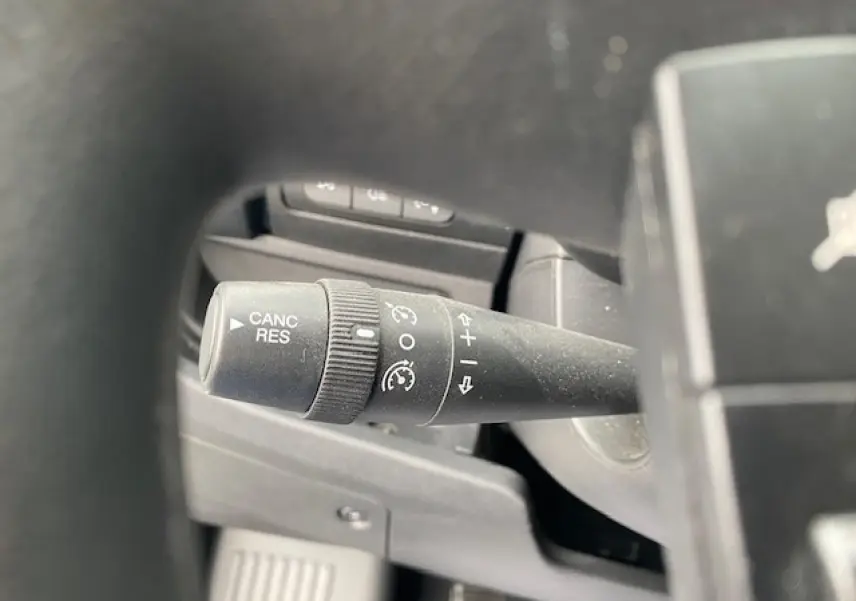 Gros plan sur la commande de régulateur de vitesse à gauche du volant dans l'habitacle du fourgon Opel Movano blanc.