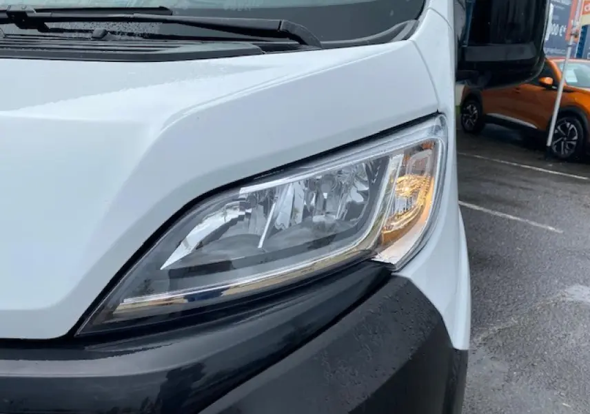 Gros plan sur le phare avant droit du fourgon blanc Opel Movano 2023, soulignant le pare-chocs noir et la carrosserie lisse.