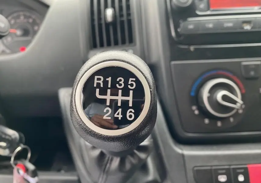 Le levier de vitesses manuel en gros plan de l'Opel Movano Fourgon blanc, avec la console de climatisation en arrière-plan.