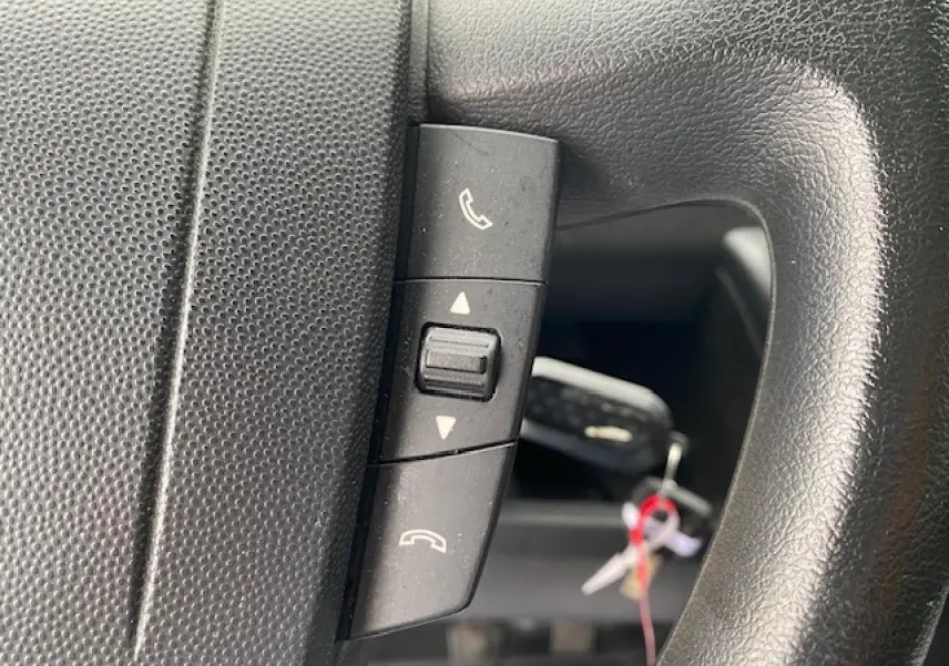 Gros plan sur les commandes Bluetooth du volant noir de l'Opel Movano Fourgon blanc 2023.