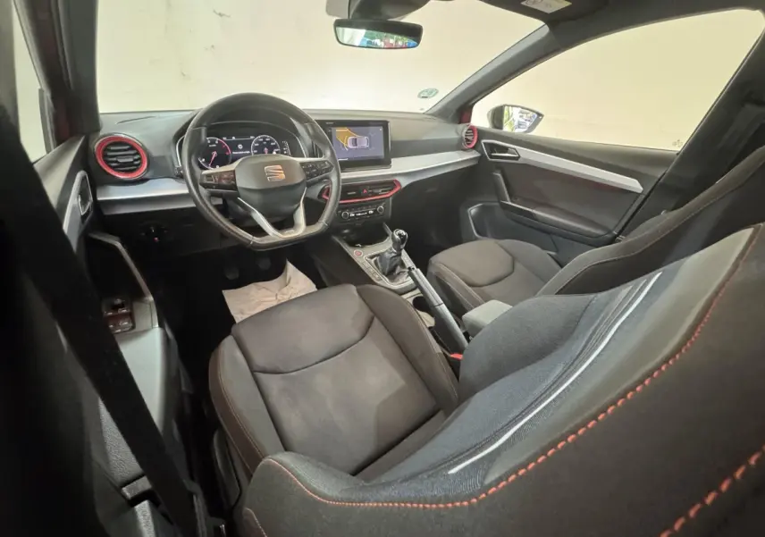 Intérieur de la SEAT Ibiza 1.0 TSI 110 FR vu côté conducteur, tableau de bord noir avec touches rouges et écran tactile.