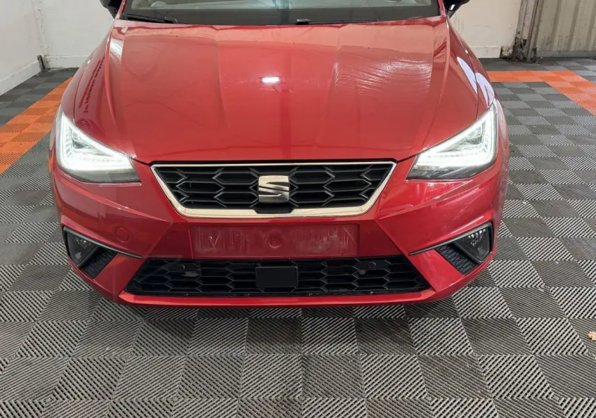 Vue de face d'une SEAT Ibiza rouge 2024 avec phares LED allumés et calandre hexagonale noire.