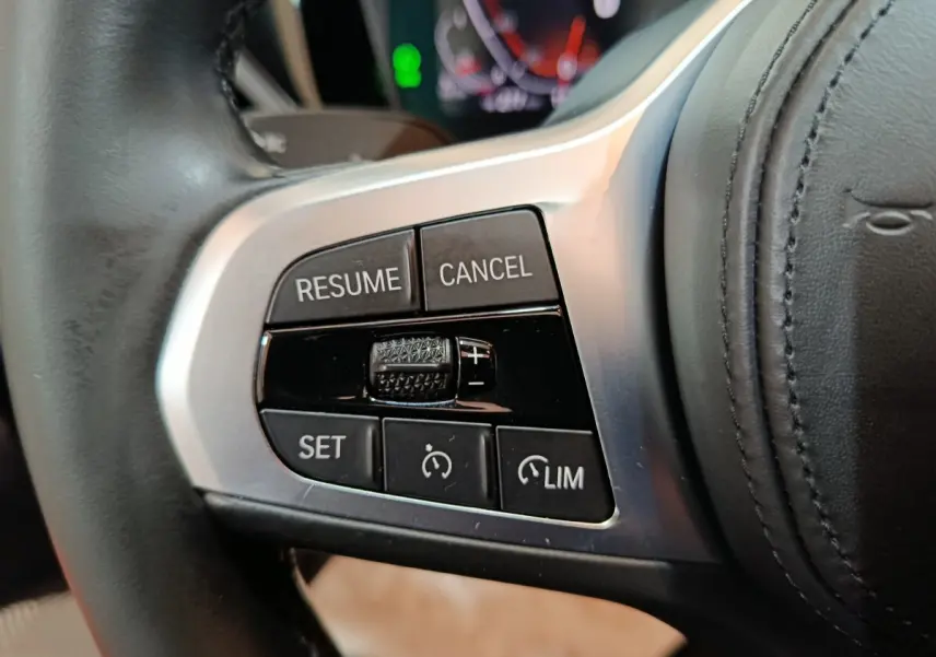 Gros plan sur les commandes de régulateur de vitesse à gauche du volant cuir d’une BMW Série 3 gris clair 2022.