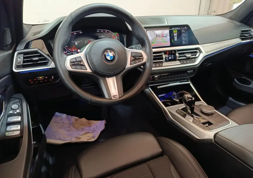 Vue intérieure avant de la BMW Série 3 318d 2022, tableau de bord noir avec écran tactile et volant cuir multifonctions.