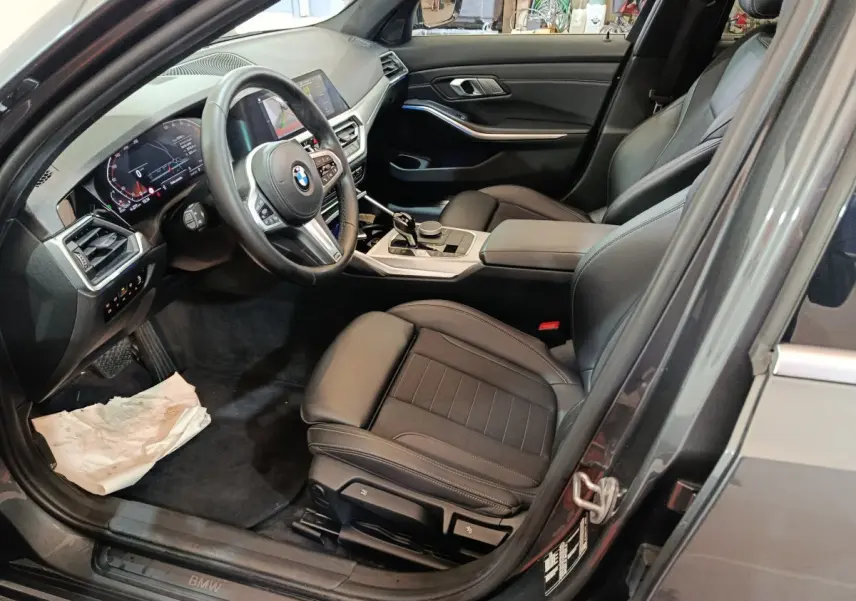 Vue intérieure côté conducteur de la BMW Série 3 318d grise, avec sièges cuir noirs et tableau de bord digital.