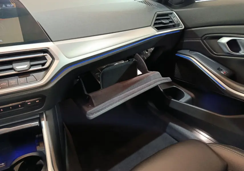 Intérieur BMW Série 3 318d 2022, vue côté passager avec boîte à gants ouverte et éclairage d’ambiance bleu.