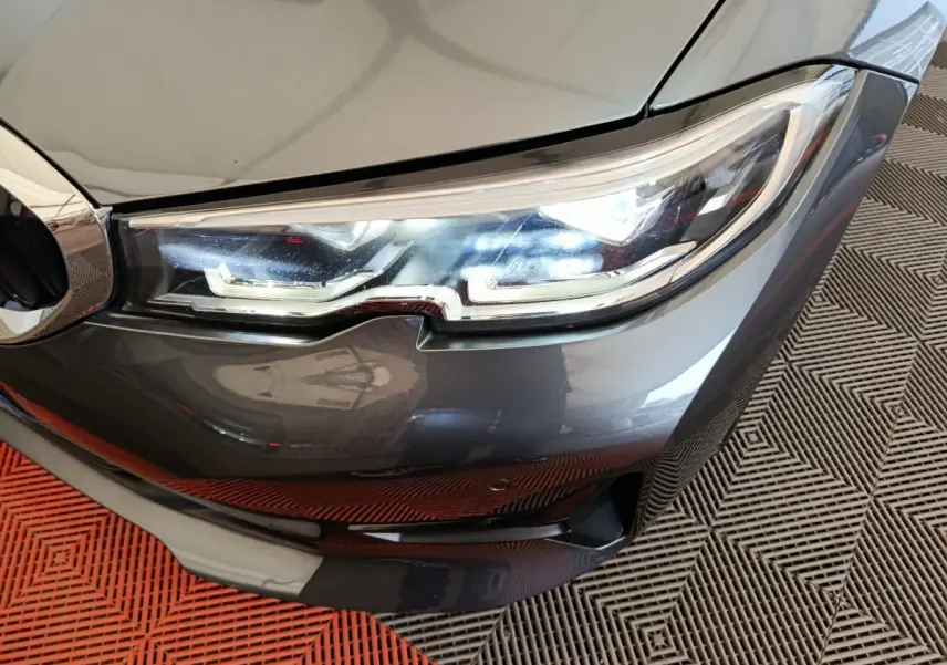 Gros plan sur le phare avant droit d'une BMW Série 3 gris clair, mettant en valeur les détails LED et la calandre.