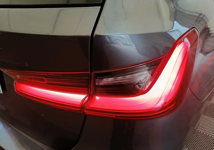 Gros plan sur le feu arrière droit rouge allumé d'une BMW Série 3 gris clair, version 318d Lounge 2022.