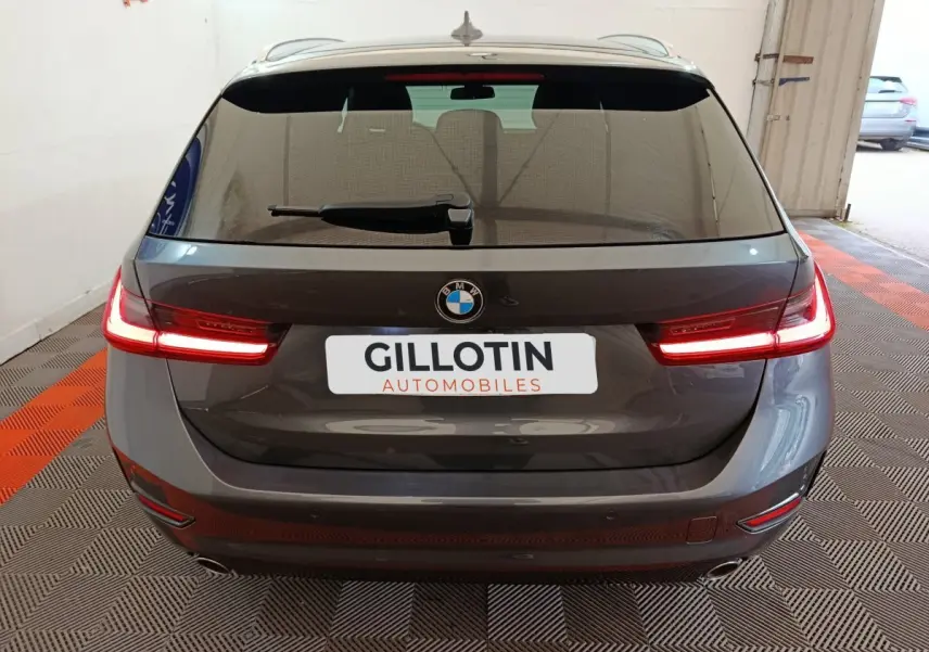 Vue arrière d'une BMW Série 3 318d gris clair avec feux LED allumés dans un garage.