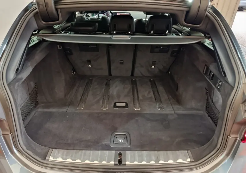 Coffre ouvert vu de l'arrière d'une BMW Série 3 318d gris clair avec intérieur noir et filet de rangement.