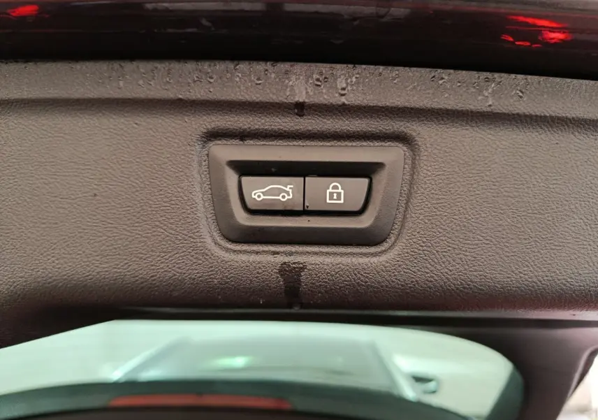 Gros plan sur les boutons d'ouverture et de verrouillage du coffre sur le hayon d'une BMW Série 3 gris clair.