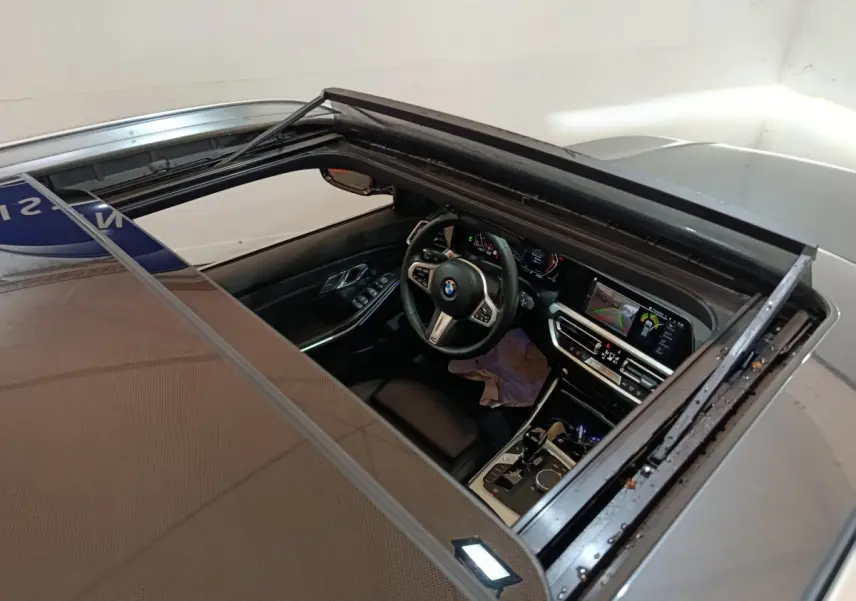 Vue plongeante sur l'intérieur noir d'une BMW Série 3 318d gris clair, avec toit ouvrant et tableau de bord digital.
