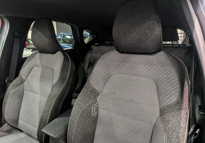 Gros plan sur les sièges avant en tissu gris du Renault Captur Mild Hybrid 2025, avec surpiqûres jaunes visibles.