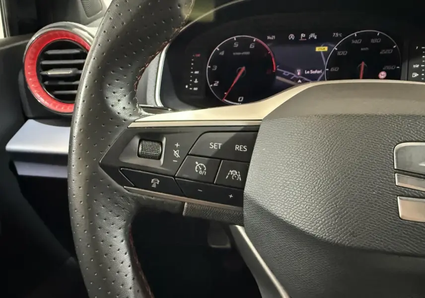 Gros plan sur le volant en cuir perforé noir de la SEAT Ibiza 2024 avec commandes multifonctions et aérateur rouge en arrière-plan.