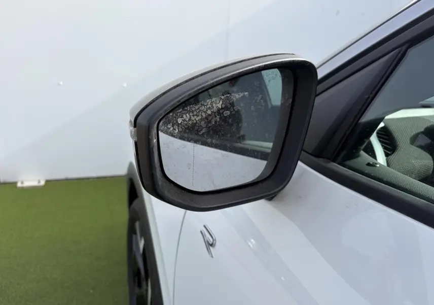 Rétroviseur côté gauche noir sur Volkswagen T-Roc blanc pur avec logo R-Line visible en gros plan.