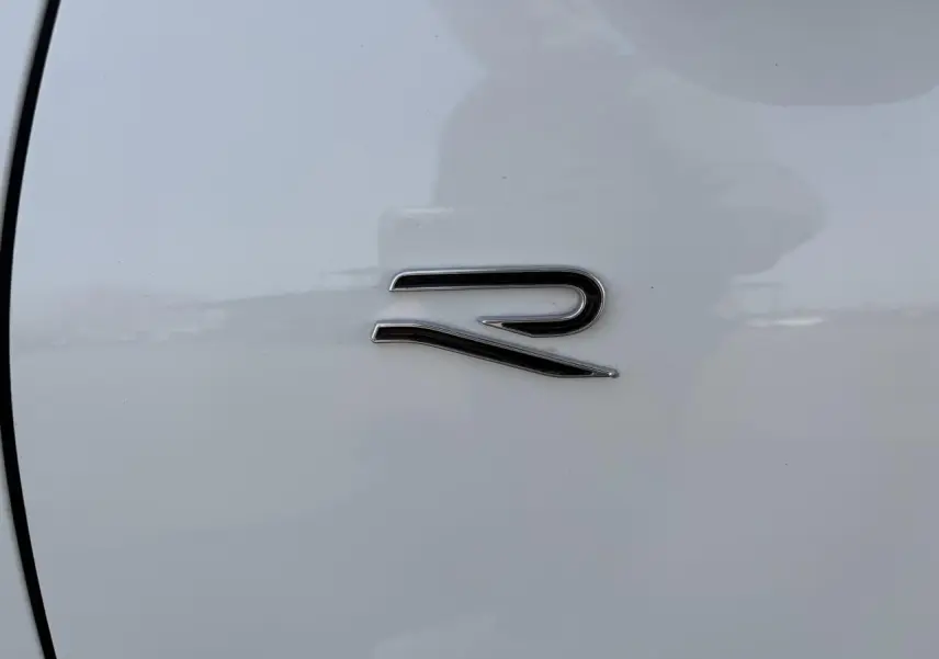 Gros plan sur l'emblème "R" chromé sur la porte blanche d'un Volkswagen T-Roc R-Line.