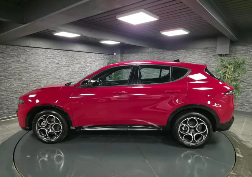 Vue de profil côté gauche d'un Alfa Romeo Tonale rouge avec jantes en alliage et détails noirs brillants.