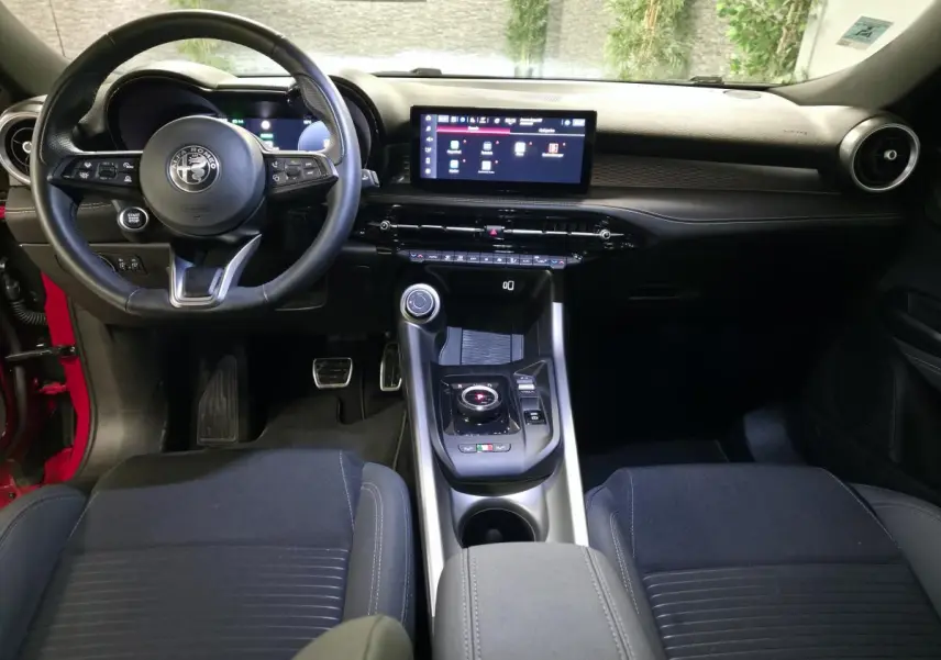 Vue intérieure avant de l'Alfa Romeo Tonale rouge 2025, avec tableau de bord noir et écran tactile central.