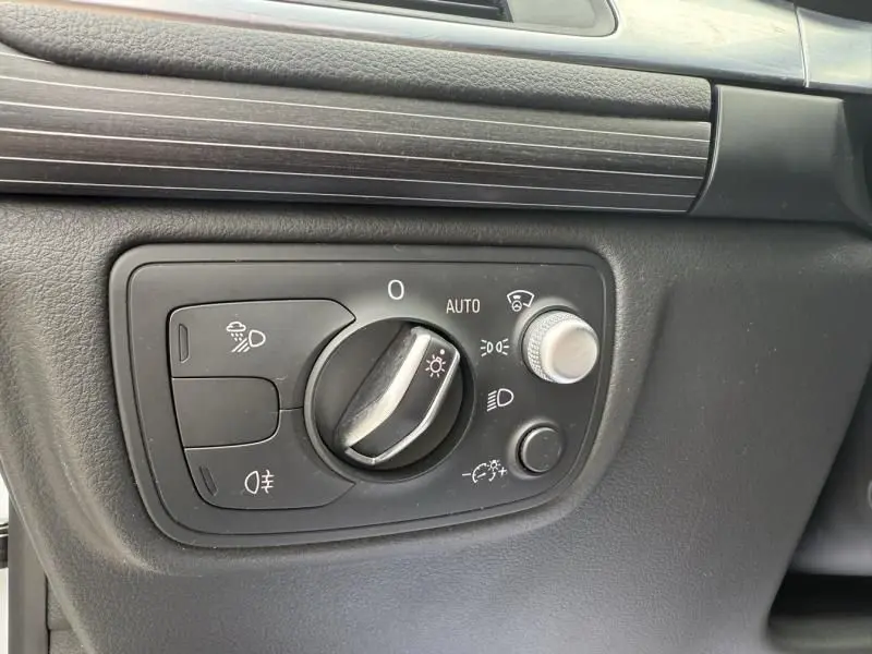 Gros plan sur le tableau de bord noir de l'Audi A7 Sportback blanc 2018, montrant la commande des phares et réglages lumineux.