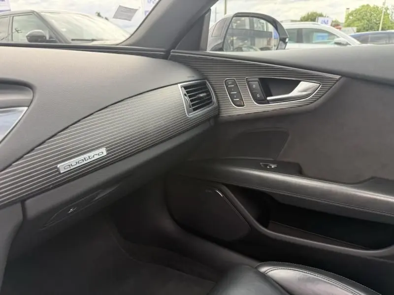 Vue intérieure côté passager de l'Audi A7 Sportback 2018 avec tableau de bord et insert décoratif Quattro en finition noire.