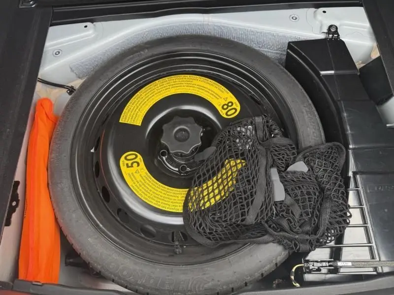 Vue rapprochée de la roue de secours noire avec étiquettes jaunes dans le coffre d'une Audi A7 Sportback blanche 2018.