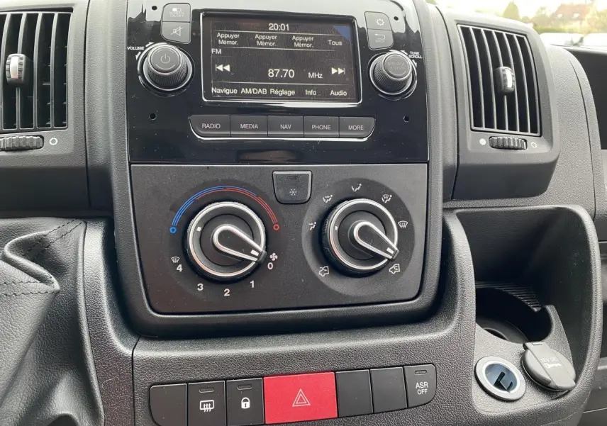 Tableau de bord central de l'Opel Movano Fourgon 2022 avec commandes climatisation, radio DAB et boutons d'alerte visibles.