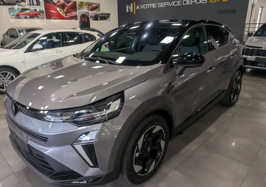 Renault Captur 2025 gris Cassiopé avec toit noir, vu en 3/4 avant droit dans un showroom lumineux.