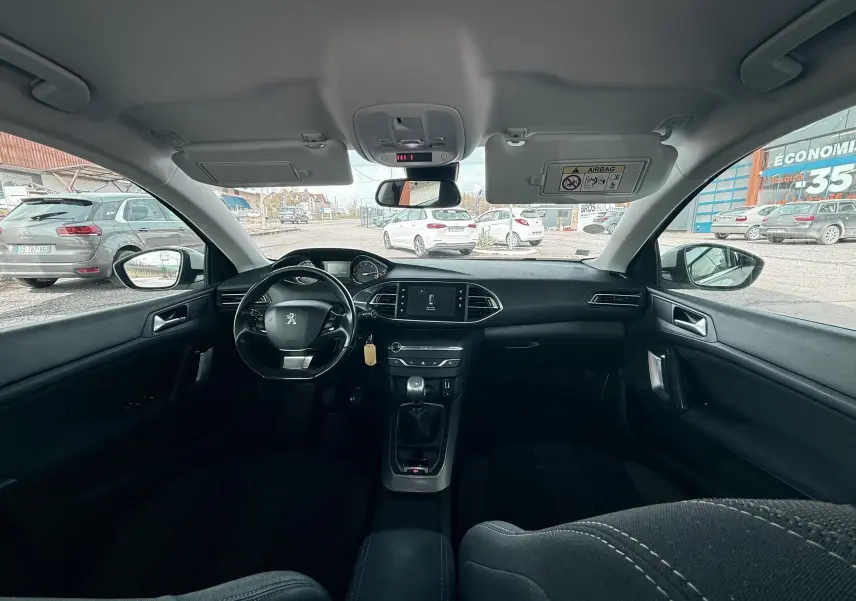 Vue intérieure avant de la Peugeot 308 2016 avec tableau de bord noir et volant multifonction.
