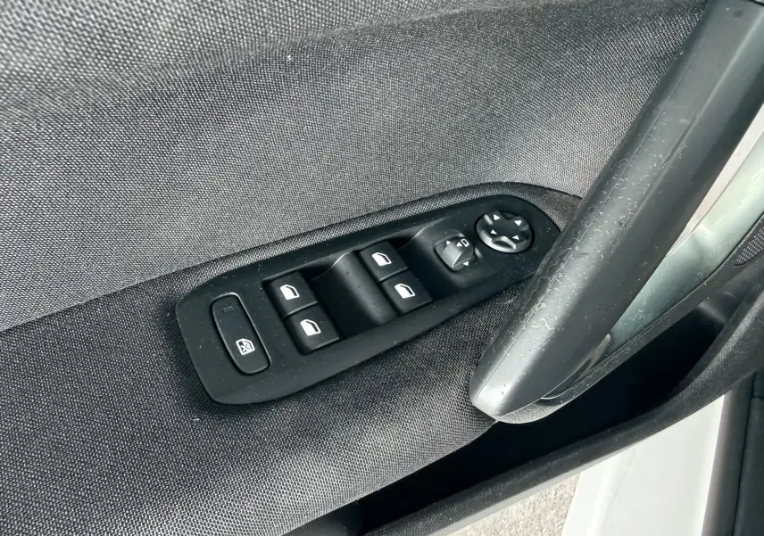 Gros plan sur les commandes de lève-vitres et rétroviseurs côté conducteur d’une Peugeot 308 blanche nacrée.