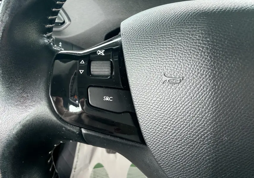 Gros plan sur les commandes noires du volant côté gauche de la Peugeot 308 blanche de 2016.