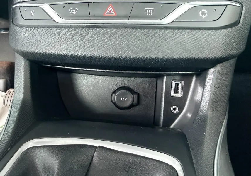 Vue rapprochée de la console centrale noire d’une Peugeot 308 avec prise 12V, port USB et boutons de commande.