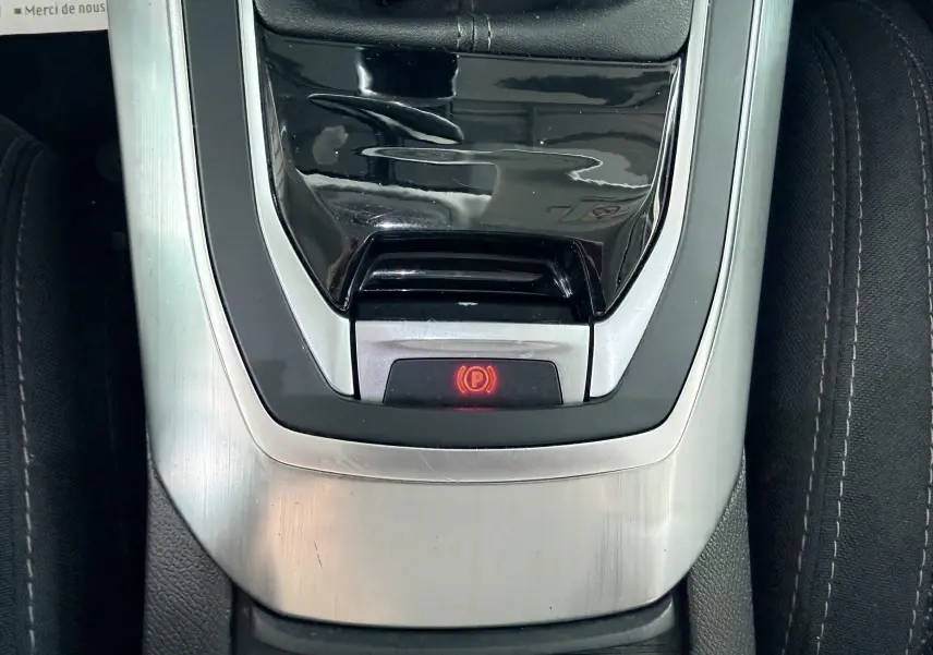 Vue rapprochée de la console centrale noire et argentée de la Peugeot 308 avec frein à main électronique allumé.