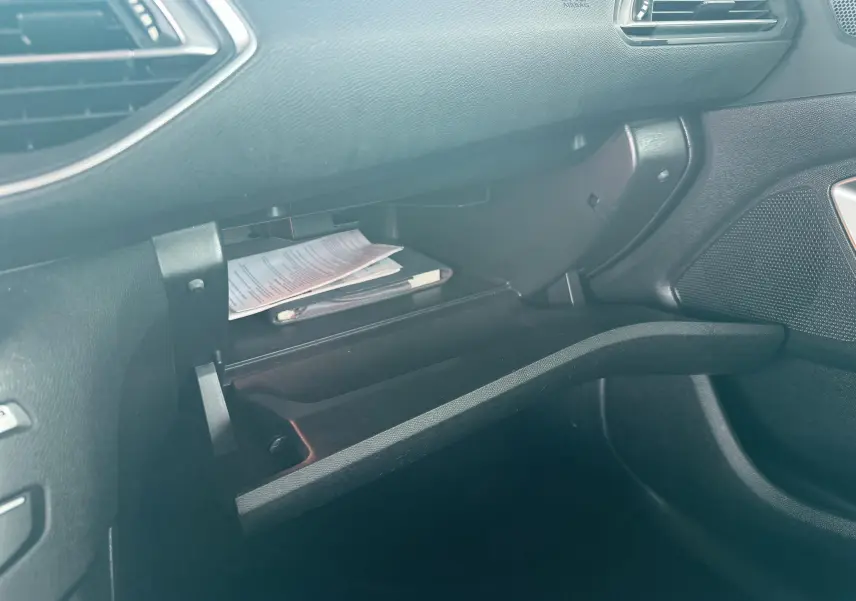 Vue intérieure côté passager du coffre à gants ouvert de la Peugeot 308, avec documents visibles à l'intérieur.