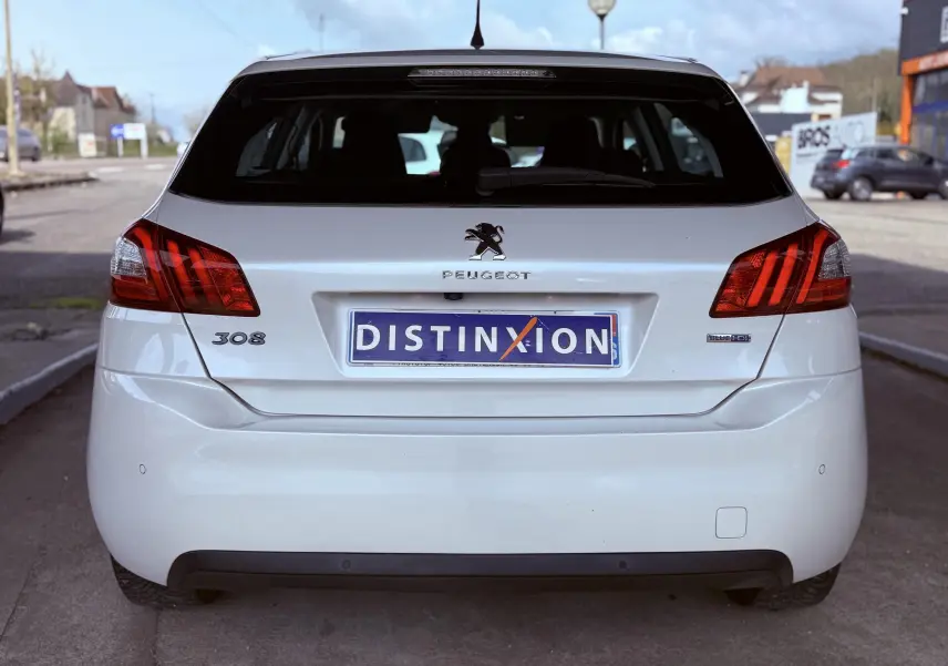 Vue arrière d’une Peugeot 308 blanche nacrée avec plaques d’immatriculation Distinxion et feux arrière rouges distinctifs.