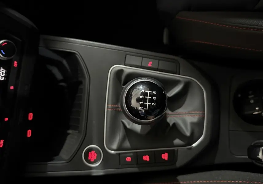 Gros plan sur le levier de vitesses manuel noir avec surpiqûres rouges dans une SEAT Ibiza 1.0 TSI 110 FR gris foncé, intérieur sombre.
