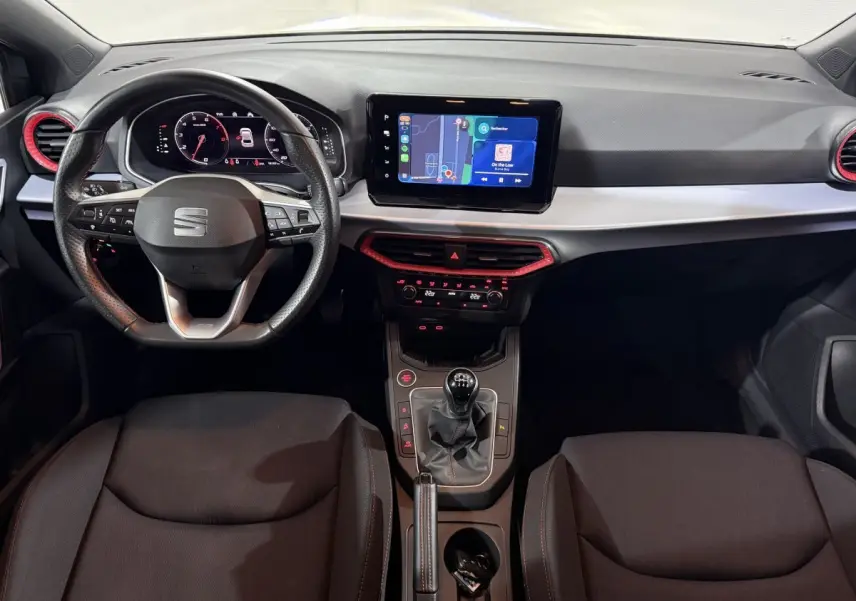 Vue intérieure frontale du tableau de bord de la SEAT Ibiza 1.0 TSI 110 FR avec volant cuir, écran tactile et détails rouges.