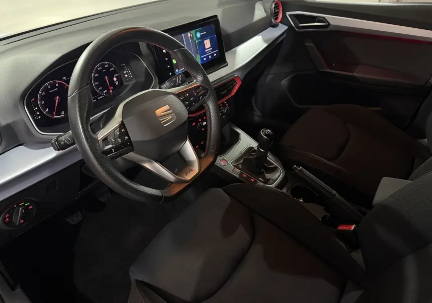 Vue intérieure côté conducteur de la SEAT Ibiza 1.0 TSI 110 FR 2024, volant cuir, écran tactile et détails rouges sur la console.