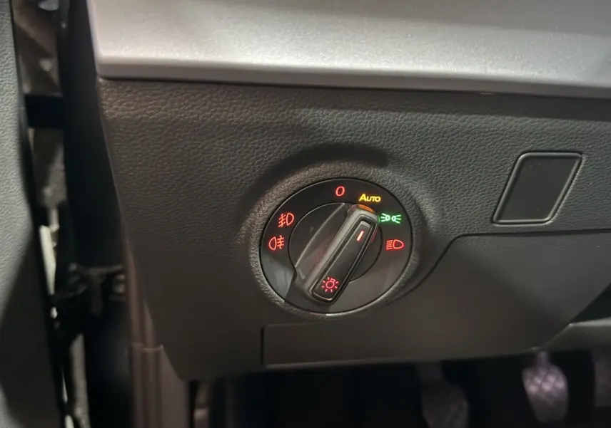 Gros plan sur le bouton de commande des phares avec réglage automatique, dans l’habitacle gris foncé de la SEAT Ibiza 2024.