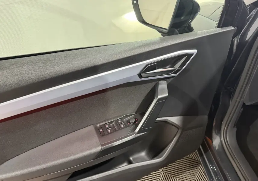 Vue intérieure côté gauche de la porte avant gris foncé de la SEAT Ibiza 1.0 TSI 110 FR avec commandes électriques et poignée argentée.