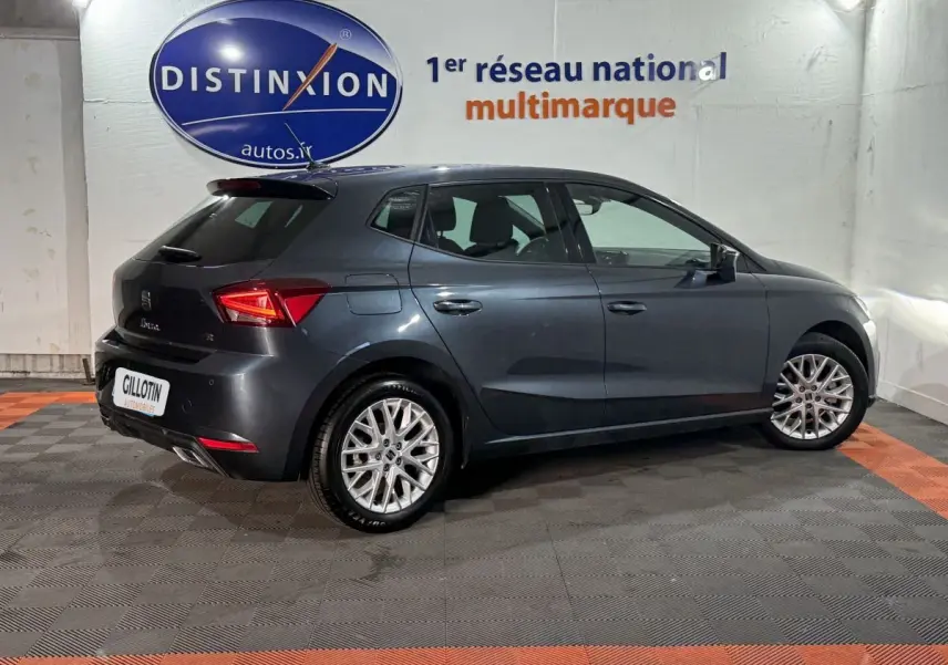 Vue 3/4 arrière droite d'une SEAT Ibiza 1.0 TSI 110 FR gris foncé, avec jantes alliage et feux LED distinctifs.