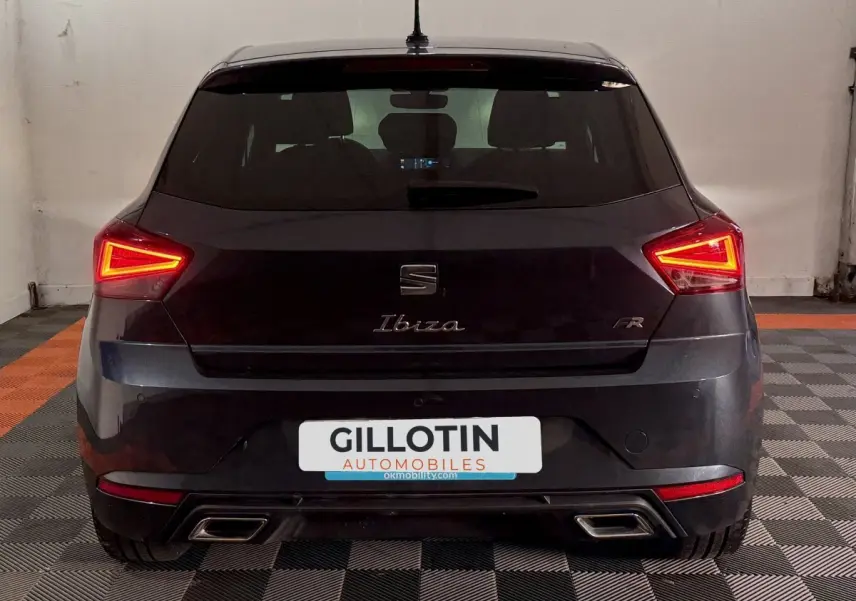 Vue arrière d'une SEAT Ibiza 1.0 TSI 110 FR gris foncé avec feux LED allumés en intérieur.
